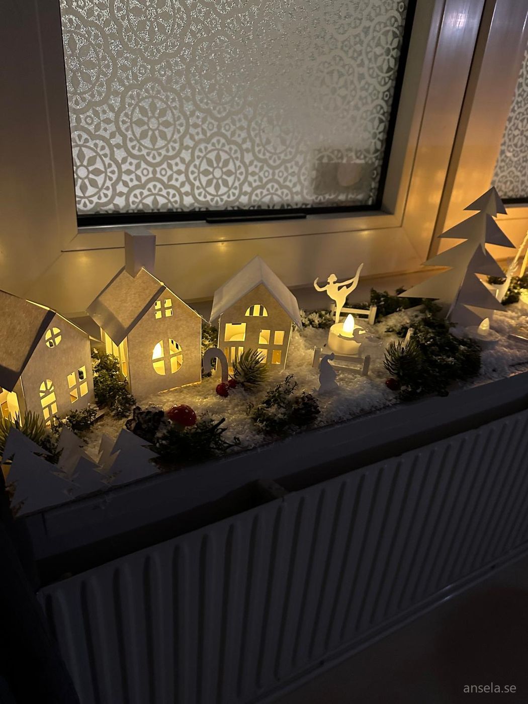Julby av papper med upplysta små hus och granar i ett fönster