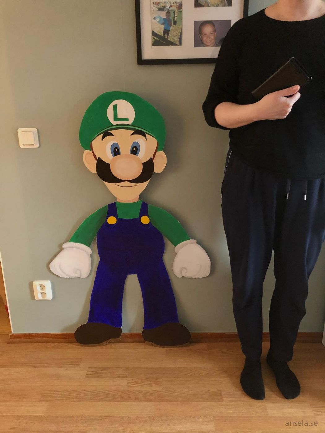 Handmålad Luigi-figur i kartong i naturlig storlek mot en vägg